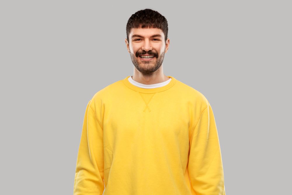 people concept - smiling young man in yellow sweatshirt over grey background. smiling young man in yellow sweatshirt