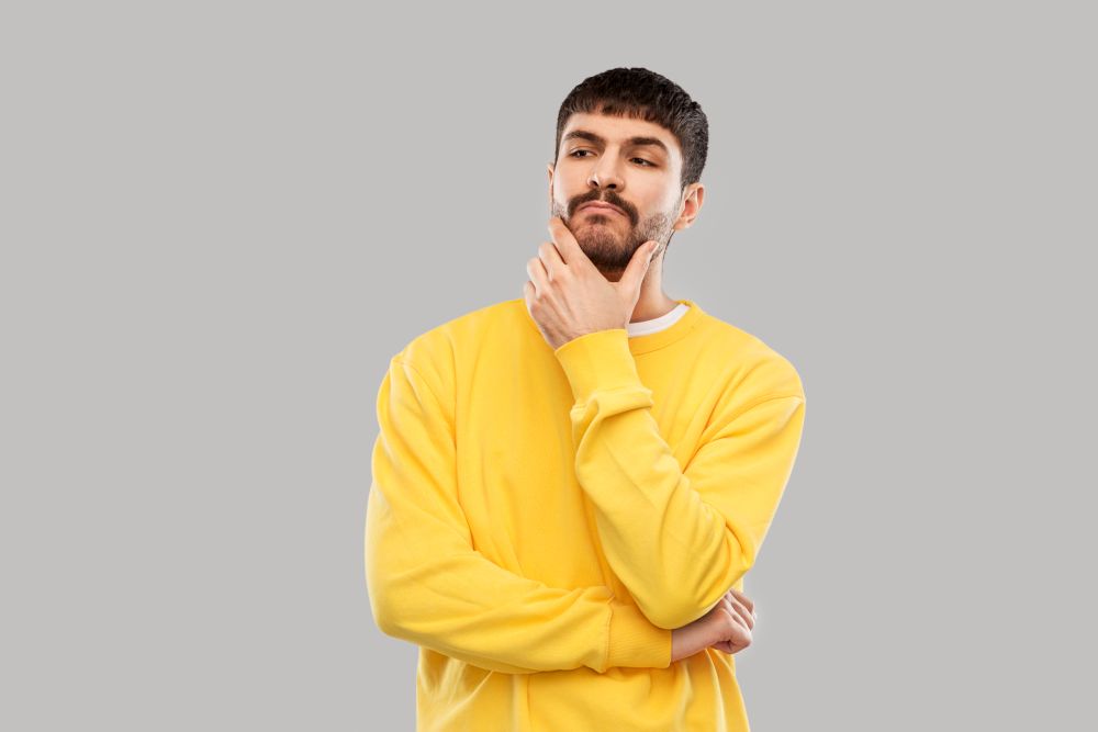 people concept - young man in yellow sweatshirt thinking over grey background. thinking young man in yellow sweatshirt