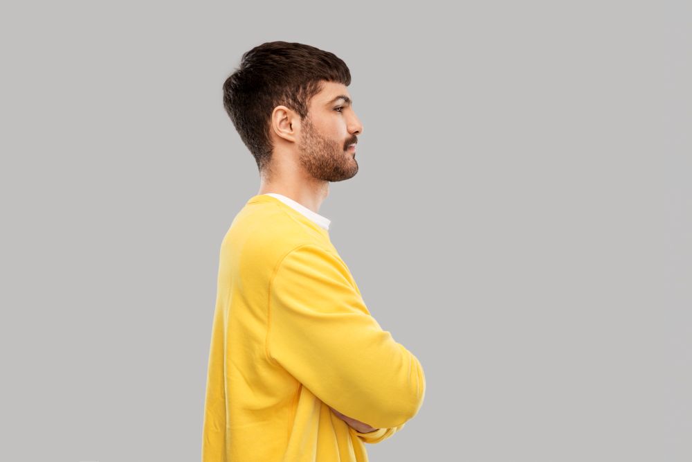 people concept - young man in yellow sweatshirt with crossed arms over grey background. young man in yellow sweatshirt with crossed arms