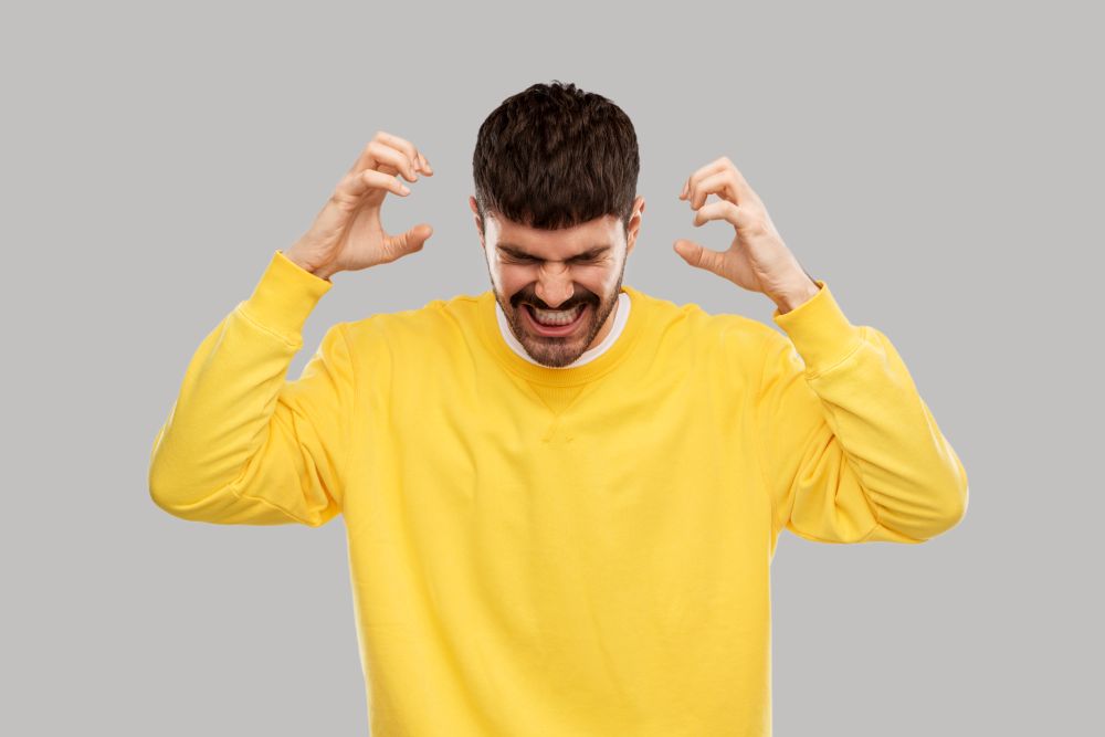 stress, emotions and people concept - angry young man in yellow sweatshirt over grey background. angry young man in yellow sweatshirt over grey