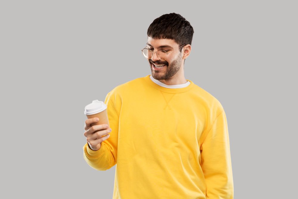drinks and people concept - smiling young man with takeaway coffee cup over grey background. smiling young man with takeaway coffee cup