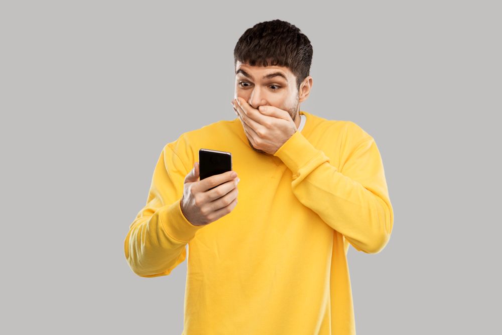 technology, communication and people concept - shocked young man with smartphone over grey background. shocked young man with smartphone