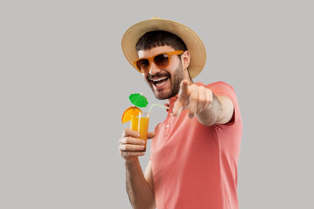 summer, vacation and people concept - happy smiling young man in sunglasses and straw hat with orange juice cocktail. happy man in straw hat with orange juice cocktail