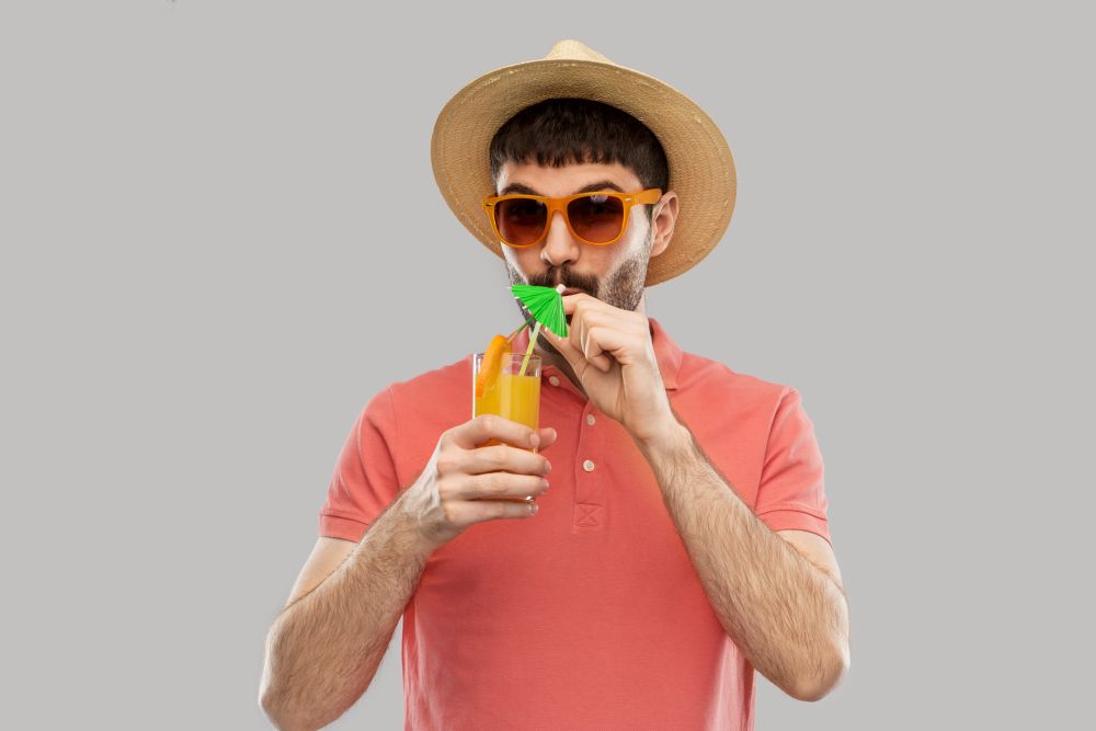 summer, vacation and people concept - happy smiling young man in sunglasses and straw hat with orange juice cocktail over grey background. happy man in straw hat with orange juice cocktail