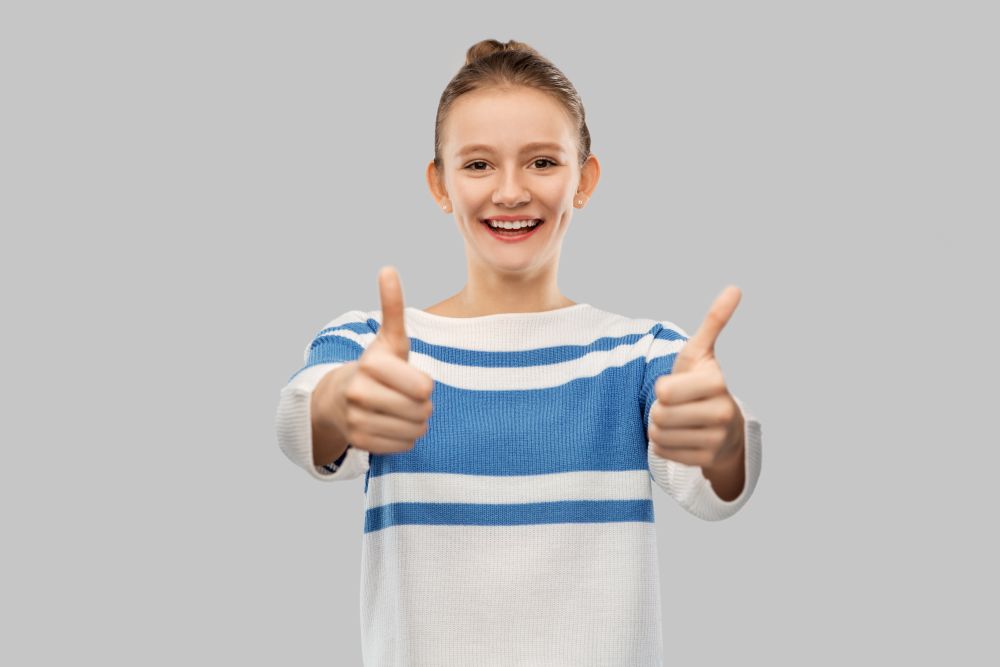 gesture and people concept - smiling teenage girl in pullover showing thumbs up over grey background. smiling teenage girl showing thumbs up
