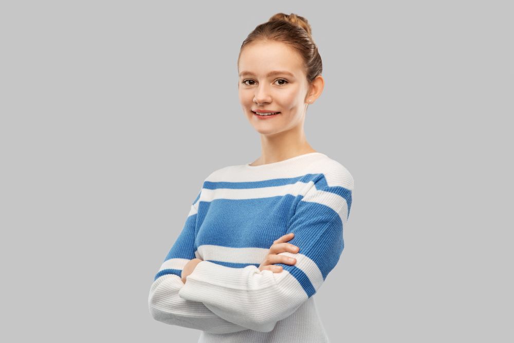 people concept - smiling teenage girl with crossed arms in pullover over grey background. smiling teenage girl with crossed arms in pullover