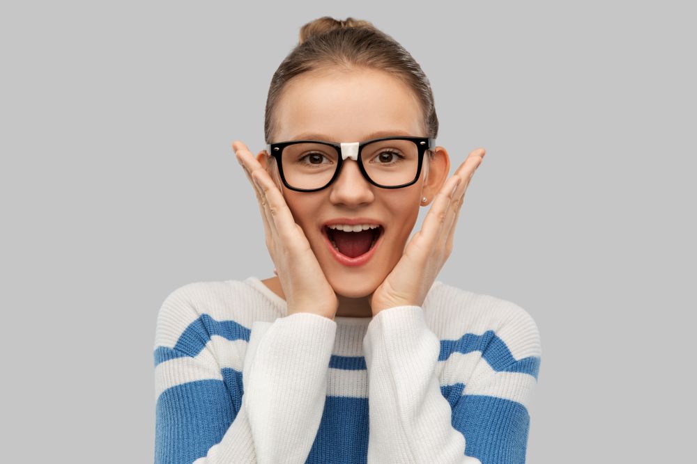 school, education and vision concept - surprised teenage student girl in taped glasses over grey background. surprised teenage student girl in taped glasses