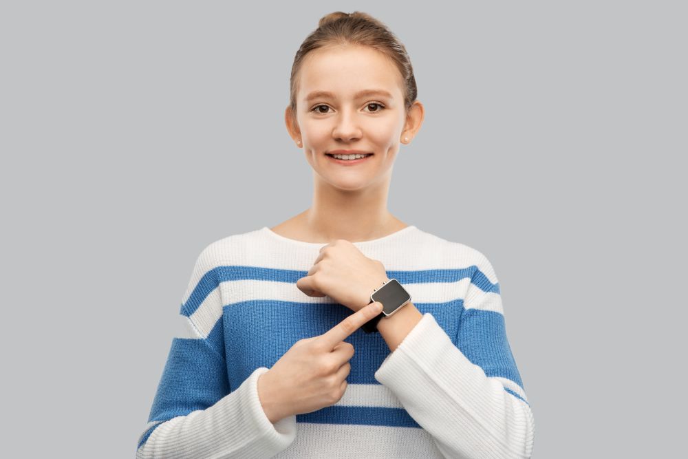 technology and people concept - happy smiling teenage girl in pullover with smart watch over grey background. happy smiling teenage girl with smart watch