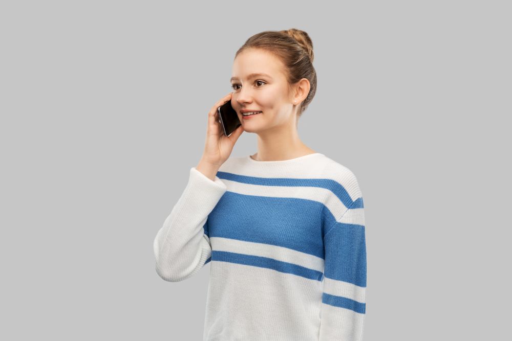 technology, communication and people concept - happy smiling teenage girl in pullover calling on smartphone over grey background. happy smiling teenage girl calling on smartphone
