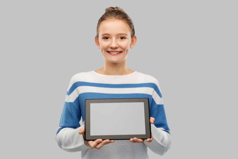 technology and people concept - happy smiling teenage girl in pullover showing tablet pc computer over grey background. happy smiling teenage girl with tablet computer