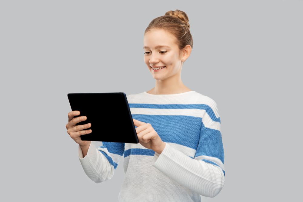 technology, communication and people concept - happy smiling teenage girl in pullover using tablet pc computer over grey background. happy smiling teenage girl using tablet computer