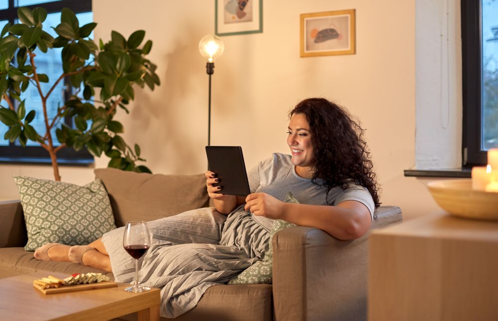 technology, leisure and people concept - happy smiling woman with tablet pc computer, red wine and snacks at home in evening. woman with tablet pc, red wine and snacks at home