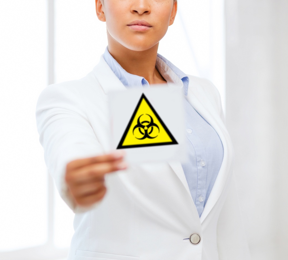 health, medicine and pandemic concept - female doctor holding boihazard caution sign. female doctor holding boihazard caution sign