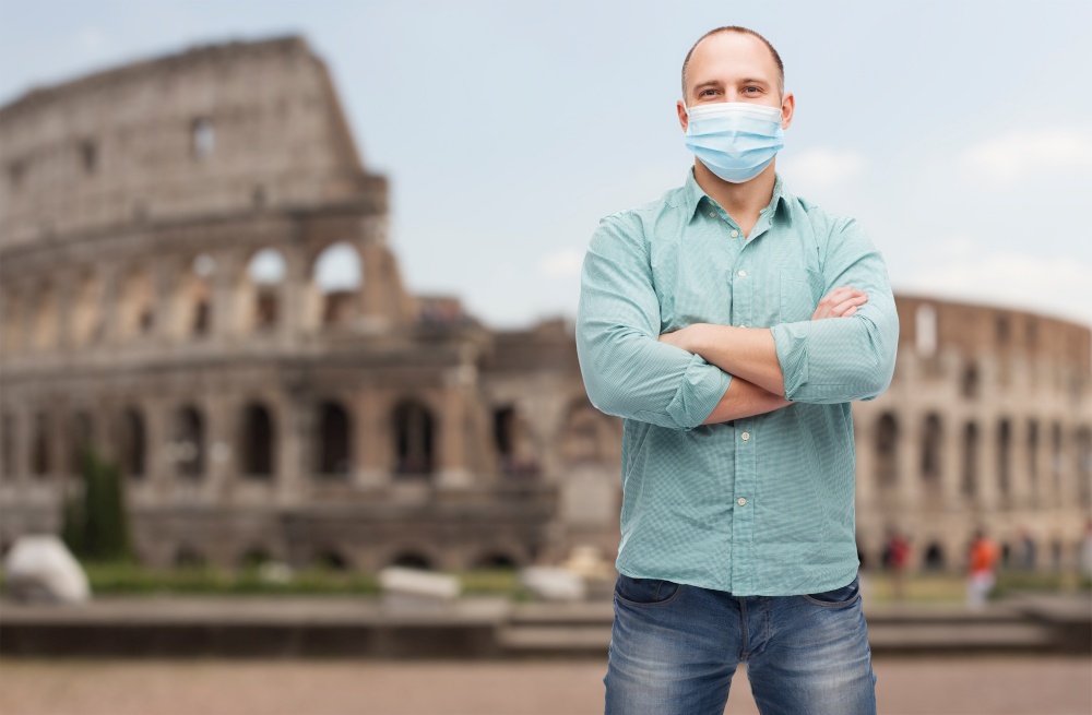 health, safety and pandemic concept - man with crossed arms wearing protective medical mask for protection from virus disease over coliseum in rome, italy background. man wearing protective medical mask in italy