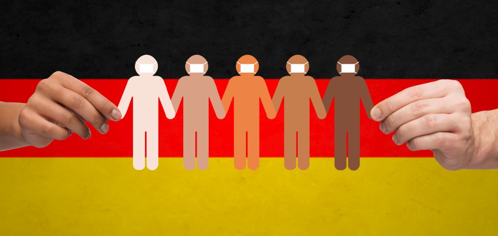 health care, social and pandemic concept - mixed-race couple&rsquo;s hands holding people chain in protective medical masks over german flag background. hands holding people chain in medical masks
