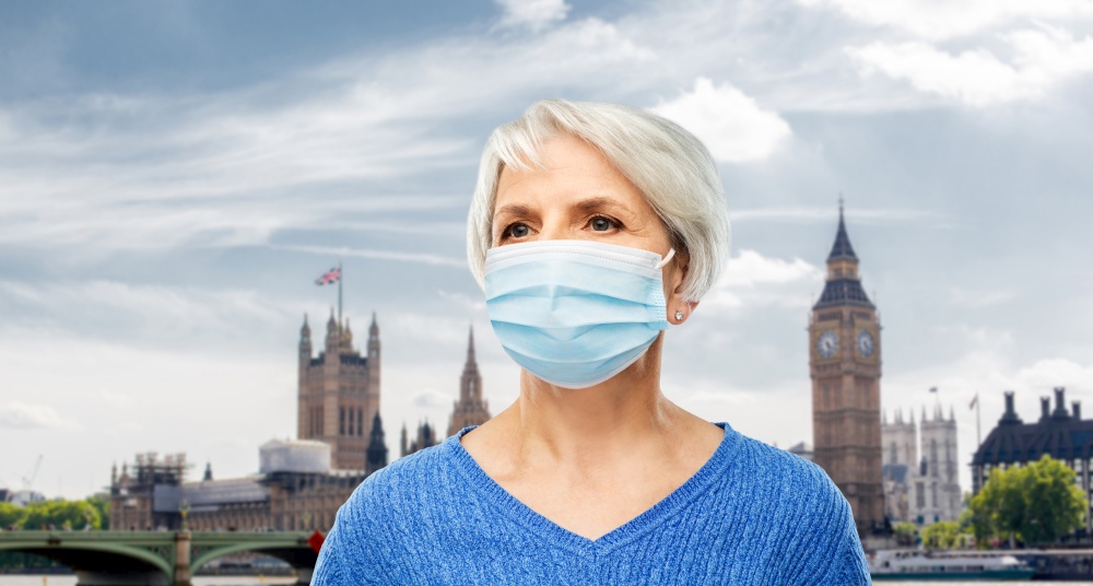 health, safety and pandemic concept - portrait of senior woman wearing protective medical mask for protection from virus over big ben in london city, england background. senior woman in protective medical mask in england