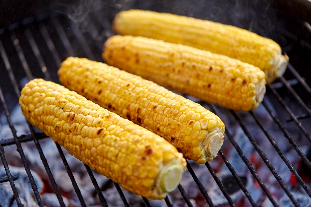 cooking, barbecue and food concept - close up of corn roasting on brazier grill outdoors. close up of corn roasting on grill