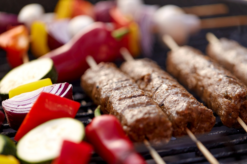 cooking, barbecue and food concept - close up of shish kebab meat and vegetables on bamboo skewers roasting to hot brazier grill outdoors. close up of barbecue kebab meat roasting on grill