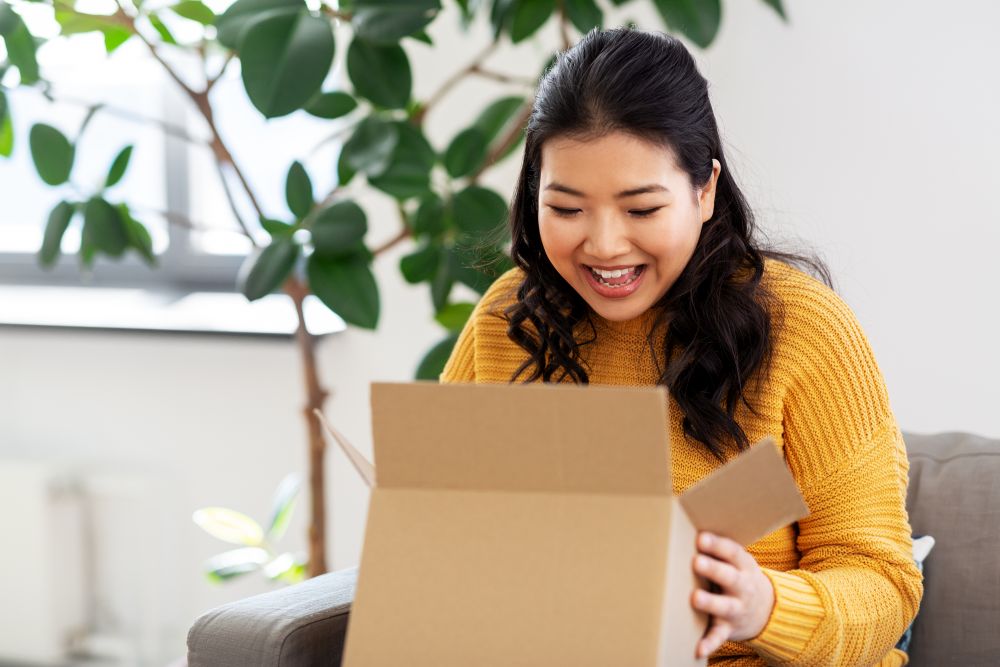 delivery, shipping and people concept - happy asian young woman with cardboard parcel box at home. happy asian young woman with parcel box at home