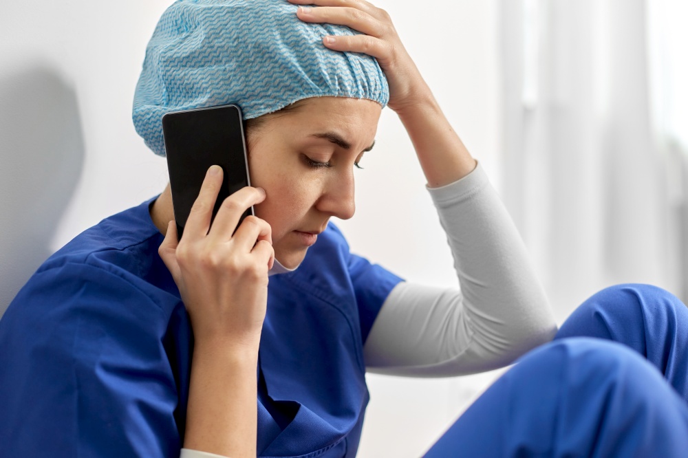 medicine, healthcare and pandemic concept - close up of sad young female doctor or nurse sitting on floor and calling on smartphone. sad doctor or nurse calling on smartphone