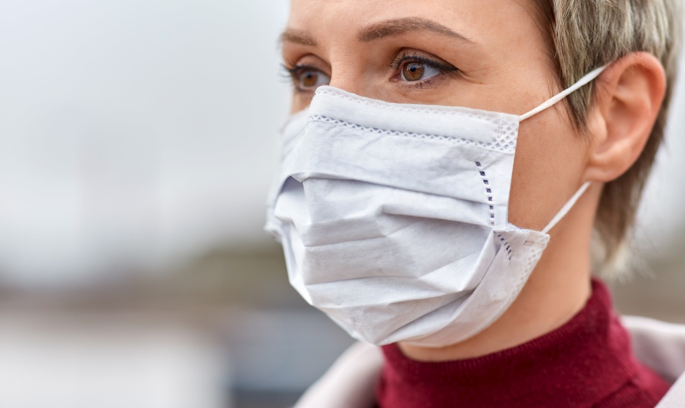 health, safety and pandemic concept - close up of young woman wearing protective medical mask outdoors. young woman wearing protective medical mask