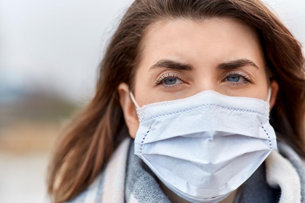 health, safety and pandemic concept - close up of young woman wearing protective medical mask outdoors. young woman wearing protective medical mask