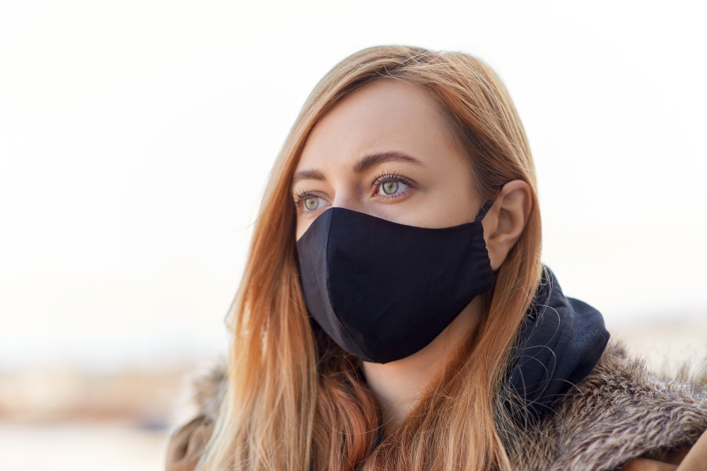 health, safety and pandemic concept - young woman wearing black face protective reusable barrier mask outdoors. woman wearing protective reusable barrier mask