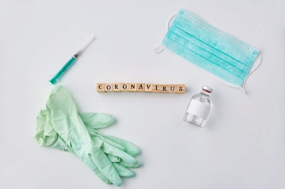 medicine, healthcare and epidemic concept - coronavirus word on wooden toy blocks , protective mask, gloves and syringe with drug on white background. coronavirus word, mask, gloves, syringe and drug