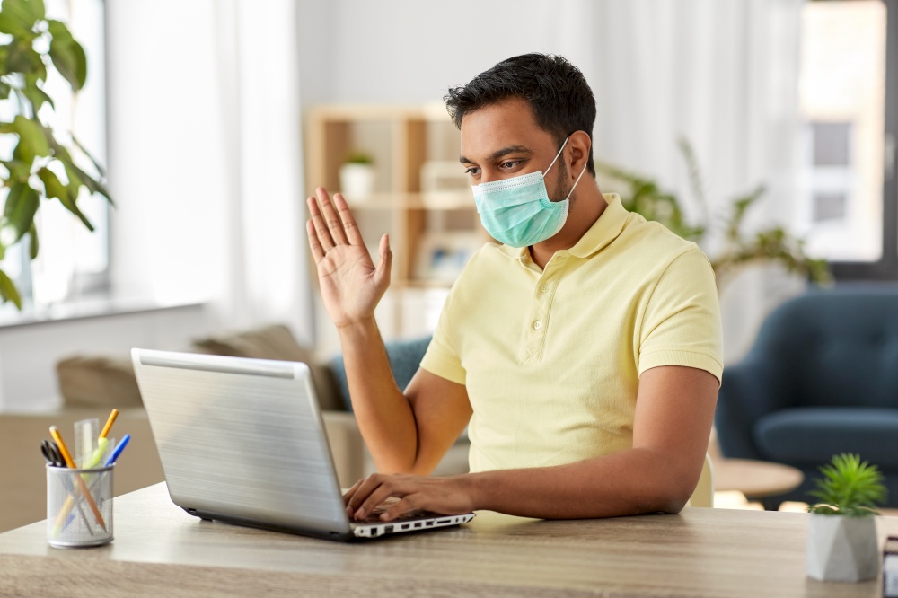quarantine, remote job and pandemic concept - indian man wearing face protective medical mask for protection from virus disease with laptop computer having video call at home office. man in mask with laptop having video call at home