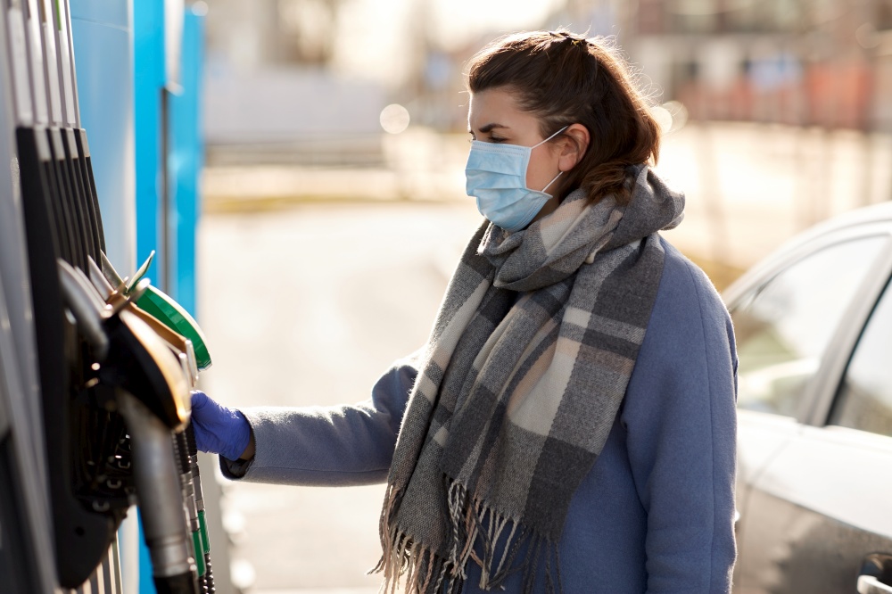 health, safety and pandemic concept - young woman wearing protective medical mask and glove taking fuel pistol at gas station. young woman wearing medical mask at gas station