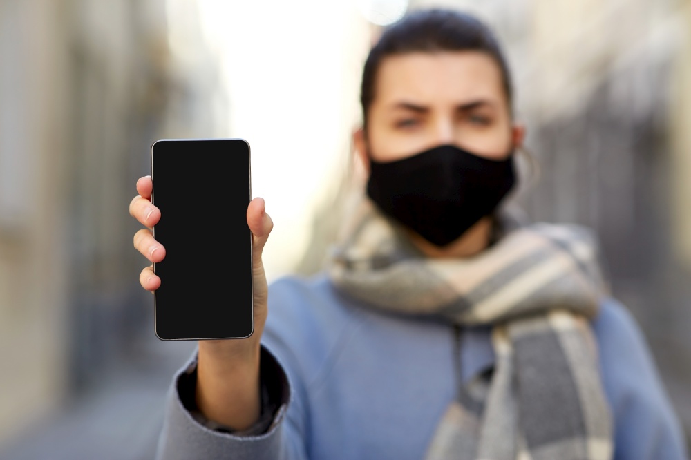 health, safety and pandemic concept - young woman wearing black face protective reusable barrier mask with smartphone outdoors. woman wearing protective reusable barrier mask