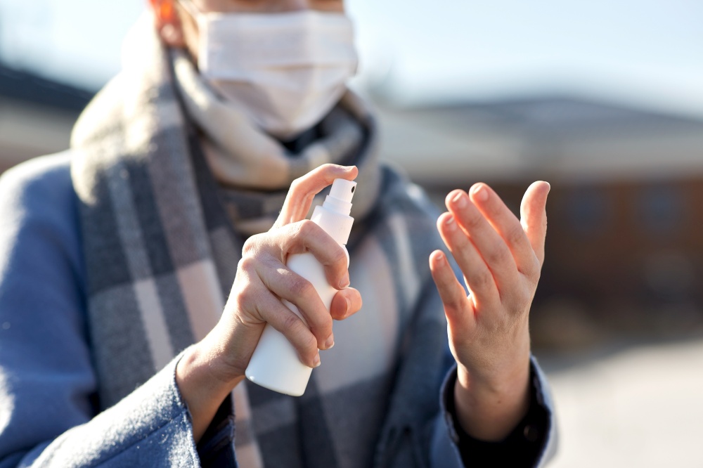 hygiene, health care and safety concept - close up of woman spraying antibacterial hand sanitizer outdoors. close up of woman spraying hand sanitizer
