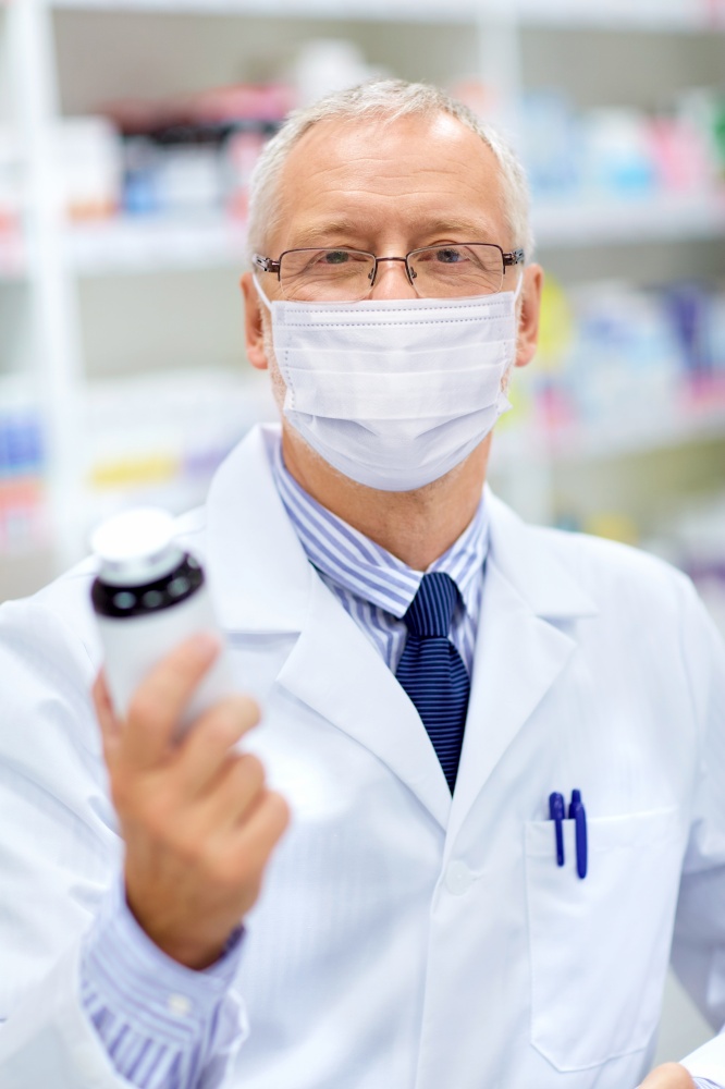 medicine, healthcare and people concept - senior apothecary wearing face protective medical mask for protection from virus disease with drug at pharmacy. old apothecary in mask with medicine at pharmacy