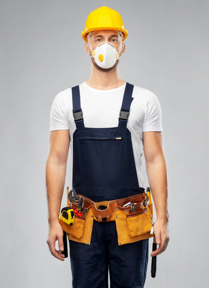 repair, construction and building - male worker or builder in helmet and respirator mask with working tools on belt over grey background. male worker or builder in helmet and respirator