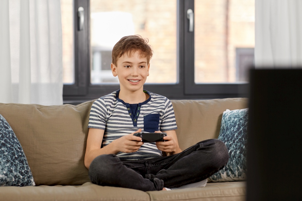 leisure, technology and children concept - smiling boy with gamepad playing video game at home. boy with gamepad playing video game at home