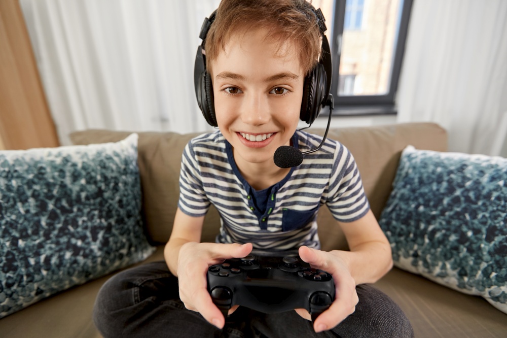 leisure, technology and children concept - smiling boy in headphones with microphone and gamepad playing video game at home. boy with gamepad playing video game at home