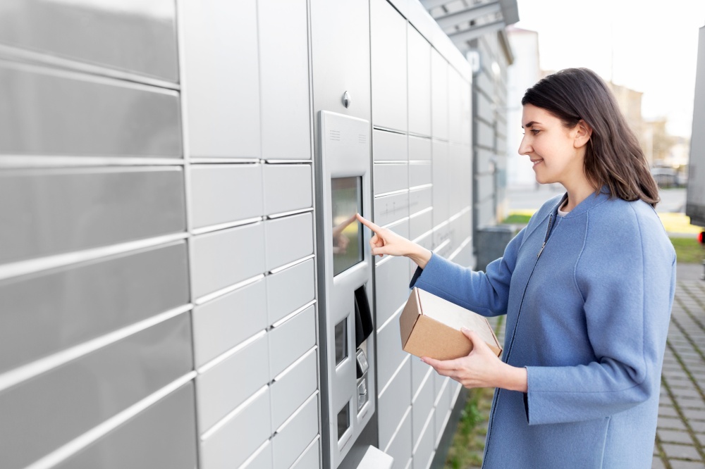 mail delivery and post service concept - happy smiling woman with box at outdoor automated parcel machine choosing operation on touch screen. smiling woman with box at automated parcel machine