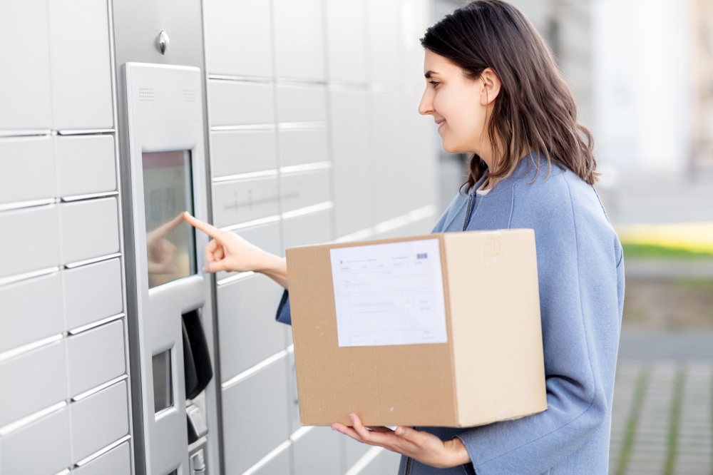 mail delivery and post service concept - happy smiling woman with box at outdoor automated parcel machine choosing operation on touch screen. smiling woman with box at automated parcel machine