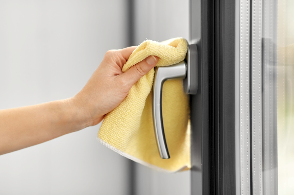 hygiene, household and cleanliness concept - close up of female hand cleaning window handle with microfiber rag. hand cleaning window handle with microfiber rag