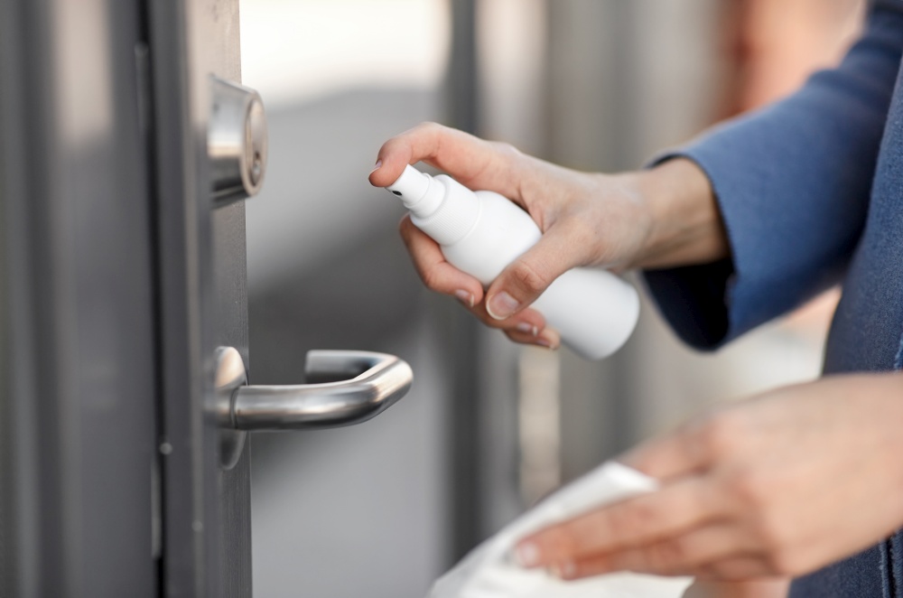 hygiene, health care and safety concept - close up of hands cleaning outdoor door handle surface with disinfectant spray and tissue. hand cleaning door handle with disinfectant spray