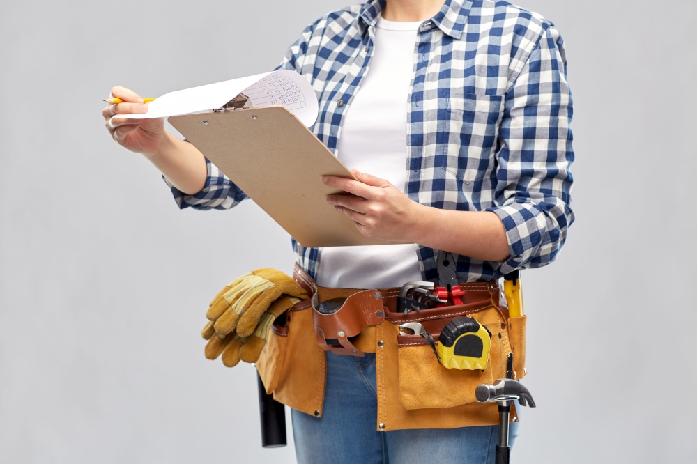 repair, construction and building concept - woman or builder with clipboard, pencil and working tools on belt over grey background. woman with clipboard, pencil and working tools