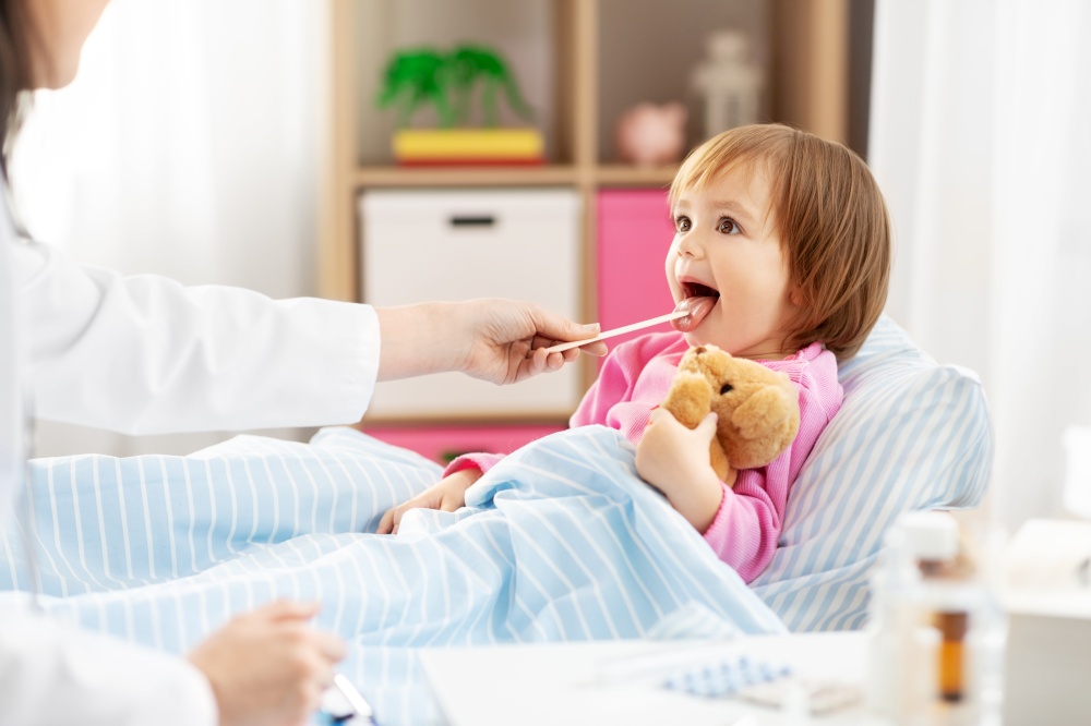 healthcare, medicine and people concept - doctor checking sick little girl&rsquo;s throat with tongue depressor in bed at home. doctor checking sick girl&rsquo;s throat at home