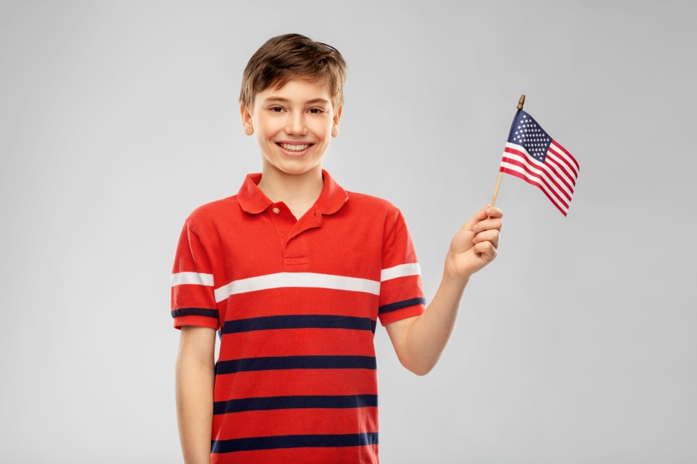 independence day, patriotism and people concept - portrait of happy smiling boy in red polo t-shirt holding flag of united states of america over grey background. portrait of happy smiling boy in red polo t-shirt