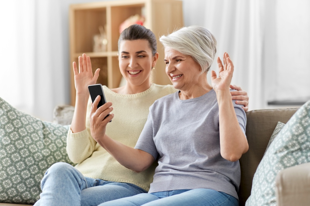 family, generation and technology concept - happy smiling senior mother and adult daughter with smartphone having video call at home. daughter and old mother having video call on phone
