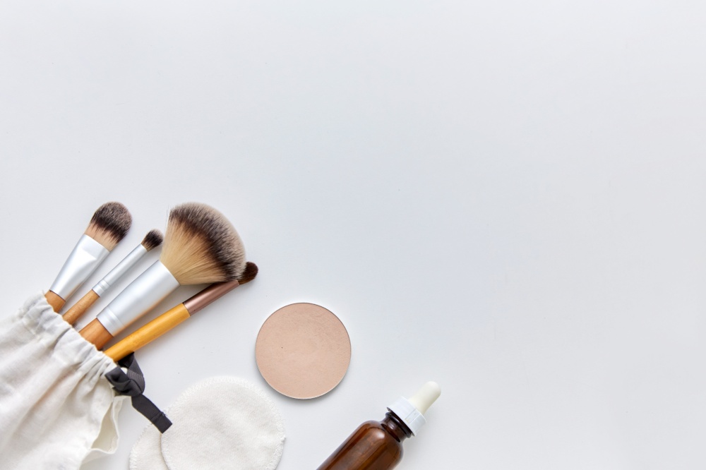 natural cosmetics and eco living concept - wooden make up brushes, cotton pads and swabs, eye shadows and essential oil or serum on white background. make up brushes, cosmetics and cotton swabs