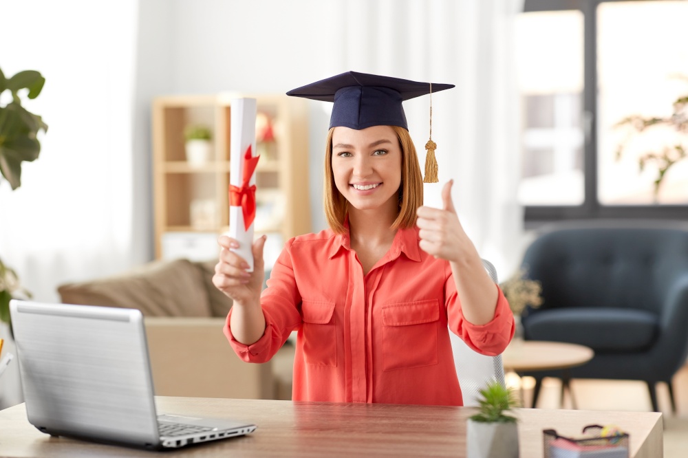 e-learning, education and people concept - happy smiling female graduate student in mortarboard with laptop computer and diploma showing thumbs up at home. student woman with laptop and diploma at home