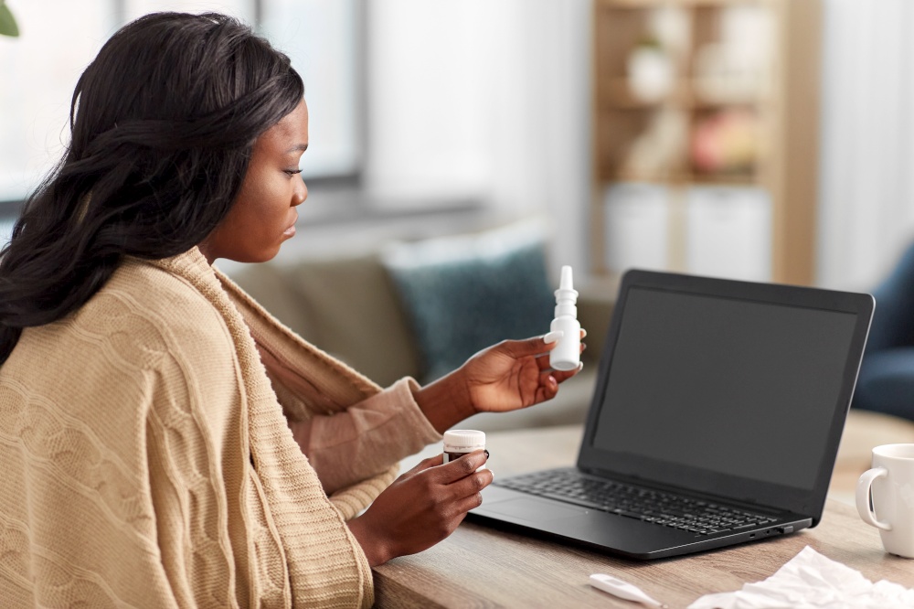 medicine, healthcare and technology concept - sick young african american woman having video call or online consultation on laptop computer at home holding drugs. sick woman having video call on laptop at home