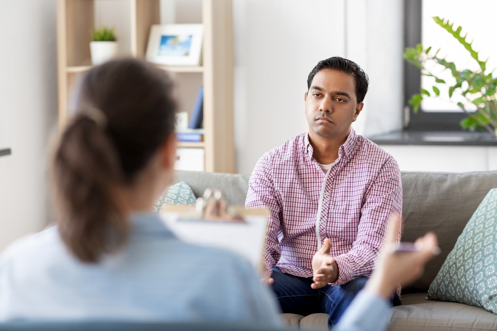 psychology, mental therapy and people concept - sad young indian man patient and woman psychologist at psychotherapy session. man and psychologist at psychotherapy session