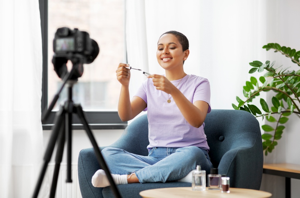 blogging, videoblog and people concept - happy smiling african american female beauty blogger with camera and make up cosmetics videoblogging at home. female beauty blogger with camera and mascara