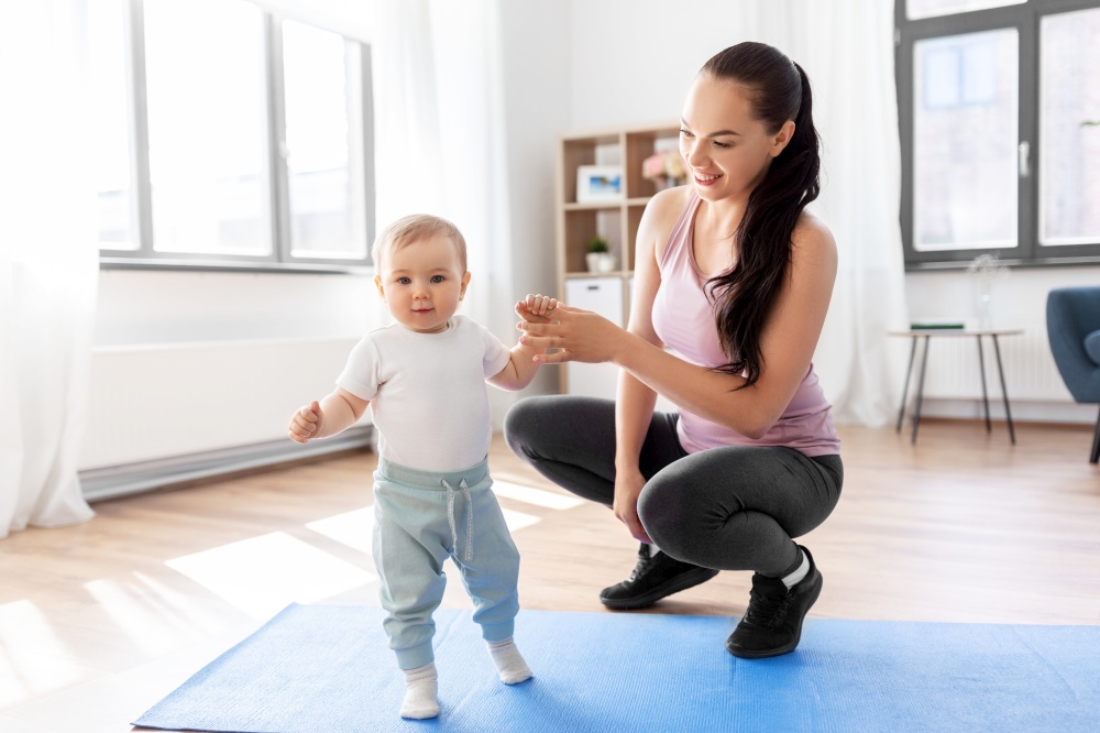 family, sport and motherhood concept - happy smiling mother with little baby sitting on exercise mat at home. happy mother with little baby at home